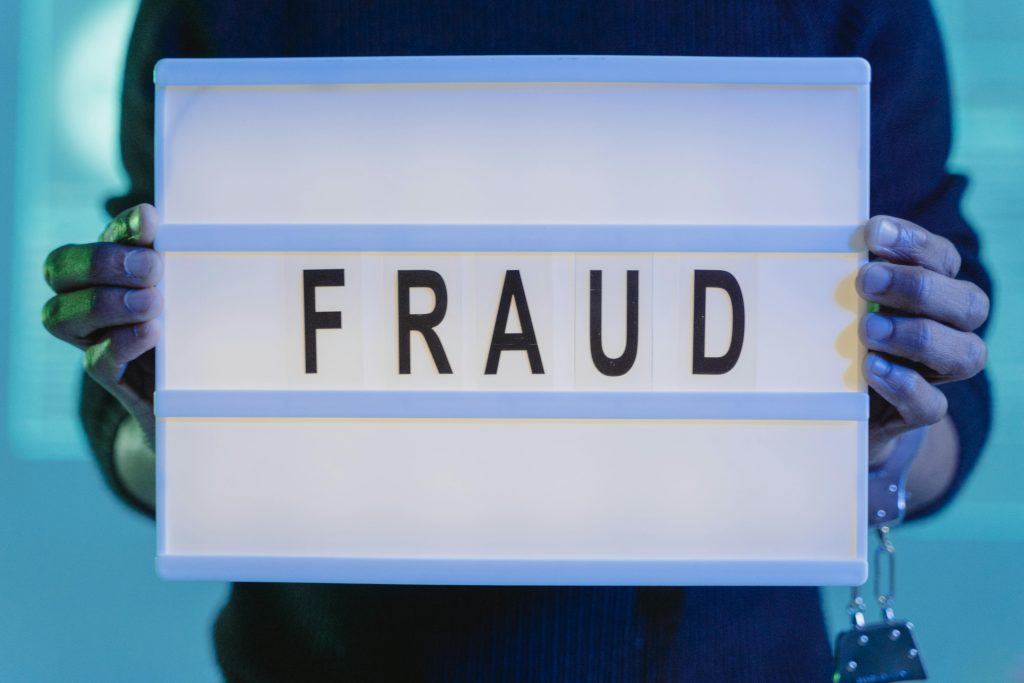 pexels-photo-6266506-6266506 Close-up of hands holding a sign with 'fraud', illuminated in blue light.