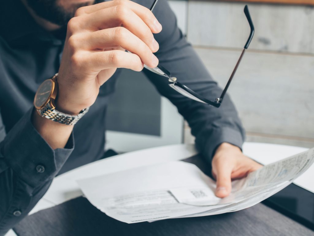 pexels-photo-7534805-7534805 Man in formal attire reviewing paperwork, holding glasses. Business setting.